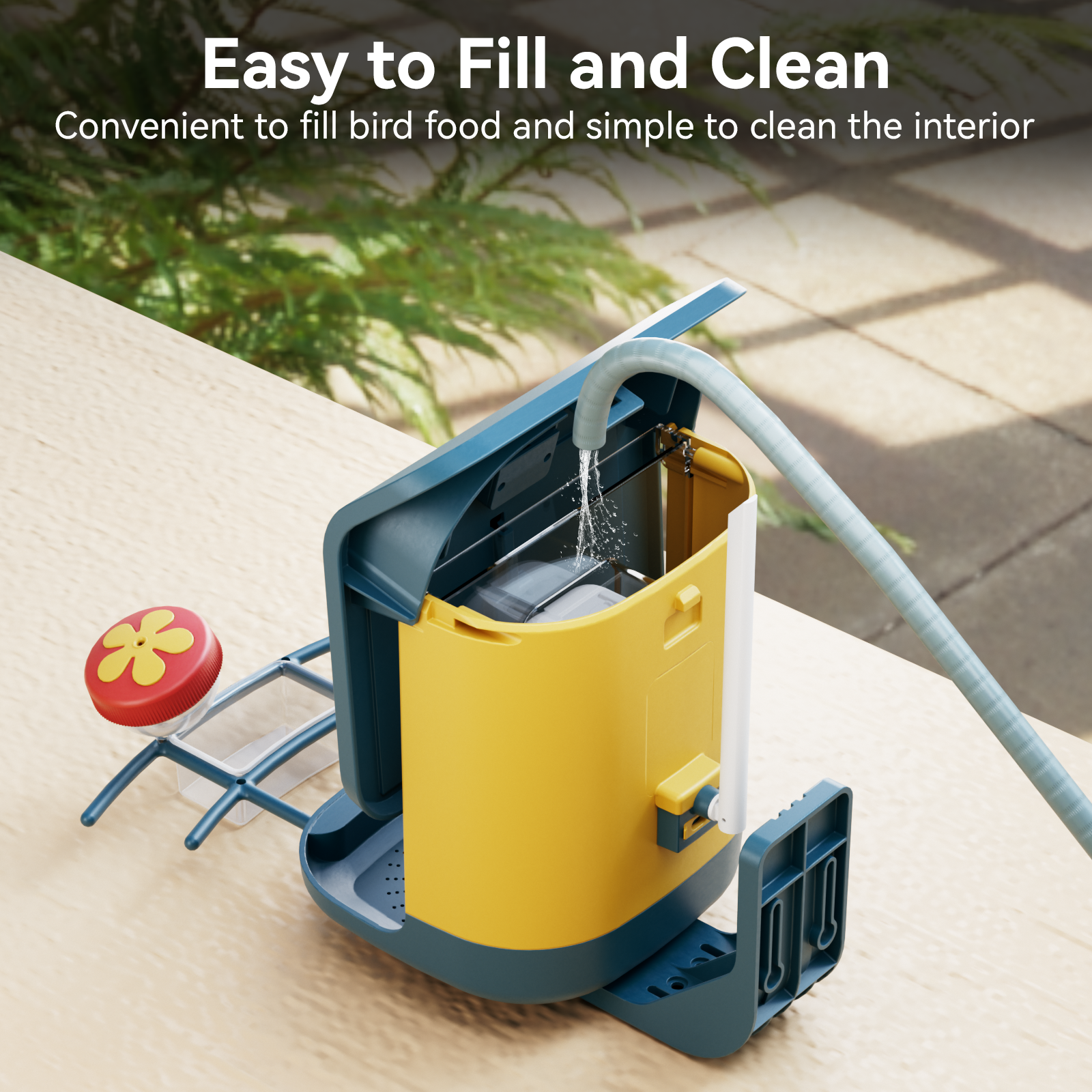 A bright yellow detachable bird seed bin from Nafnti being washed with a water hose for easy cleaning.